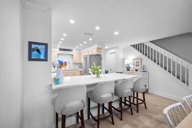 kitchen featuring kitchen peninsula, high end fridge, light brown cabinets, light hardwood / wood-style flooring, and a breakfast bar area