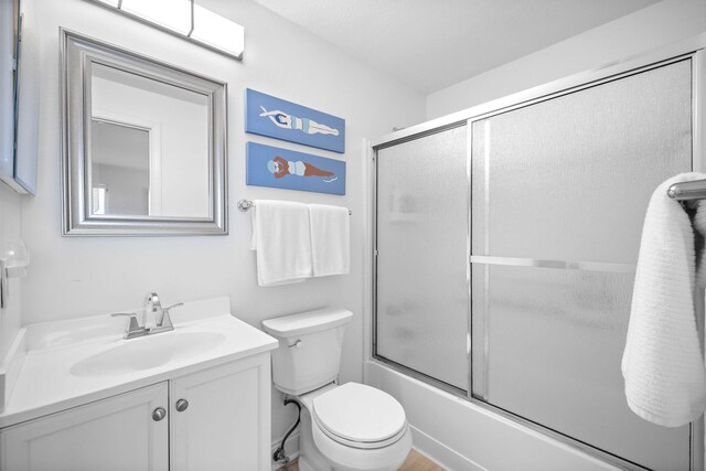 full bathroom with combined bath / shower with glass door, vanity, and toilet