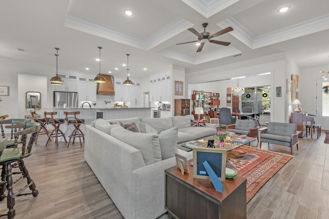 living room featuring coffered ceiling, crown molding, light wood-type flooring, beam ceiling, and ceiling fan with notable chandelier