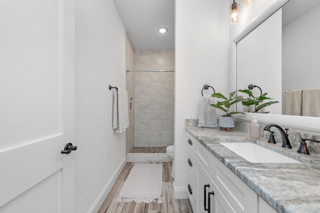 bathroom featuring vanity, hardwood / wood-style floors, toilet, and tiled shower