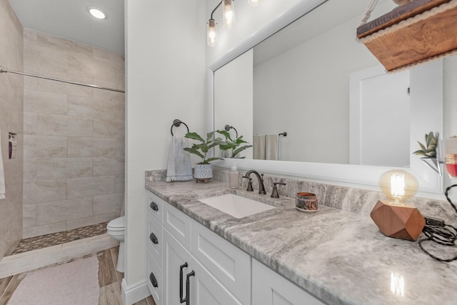 bathroom featuring vanity, a tile shower, and toilet