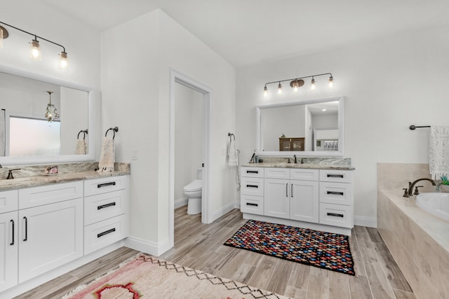 bathroom featuring tiled tub, vanity, hardwood / wood-style floors, and toilet