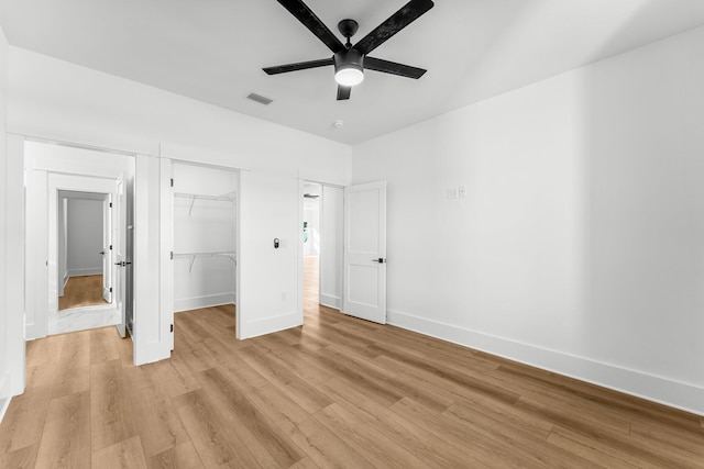 unfurnished bedroom with a walk in closet, a closet, light hardwood / wood-style flooring, and ceiling fan