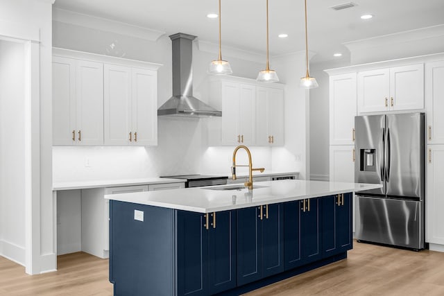 kitchen with stainless steel fridge, a kitchen island with sink, hanging light fixtures, and wall chimney range hood