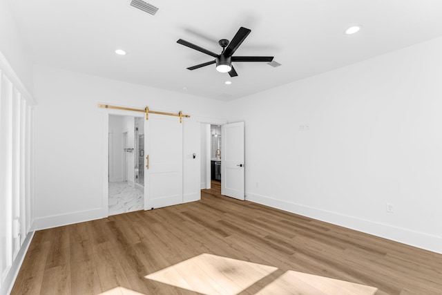 unfurnished bedroom featuring a barn door, ceiling fan, and light hardwood / wood-style floors