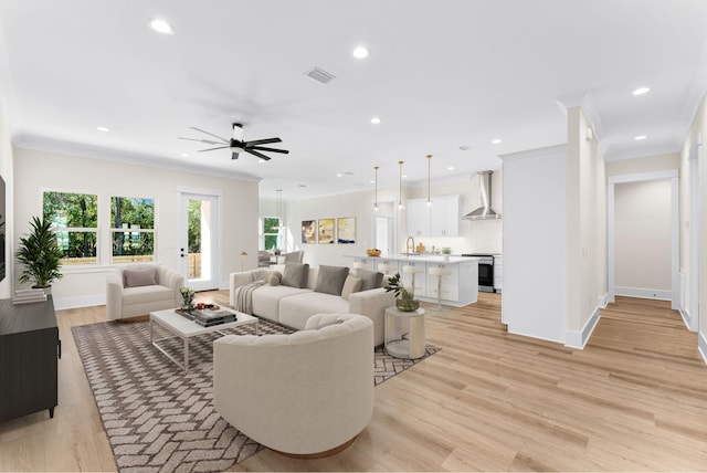 living room with crown molding, sink, ceiling fan, and light wood-type flooring