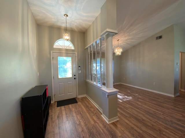 entrance foyer featuring decorative columns, dark wood-type flooring, a chandelier, and lofted ceiling