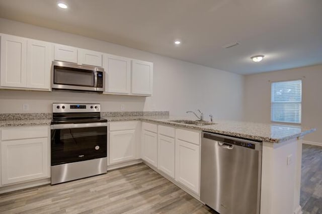 kitchen with kitchen peninsula, appliances with stainless steel finishes, light wood-type flooring, sink, and white cabinets