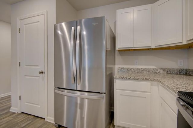 kitchen with stainless steel fridge, light stone countertops, white cabinetry, and light hardwood / wood-style flooring