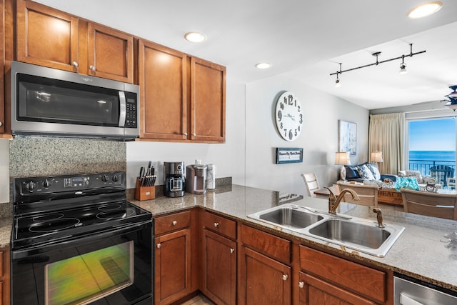 kitchen featuring sink, rail lighting, stainless steel appliances, dark stone countertops, and decorative backsplash