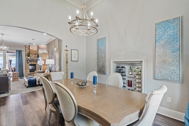 dining room featuring dark hardwood / wood-style flooring, a stone fireplace, crown molding, and a notable chandelier