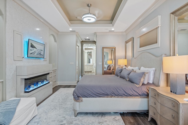 bedroom with connected bathroom, ceiling fan, dark wood-type flooring, crown molding, and a tray ceiling