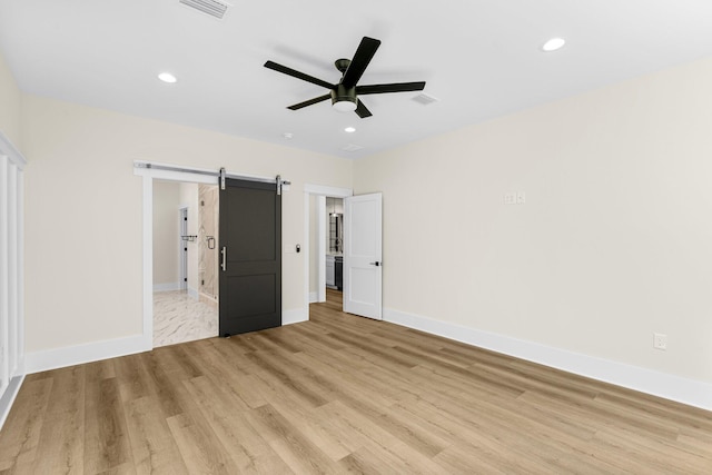 unfurnished bedroom featuring ceiling fan, a barn door, and light wood-type flooring