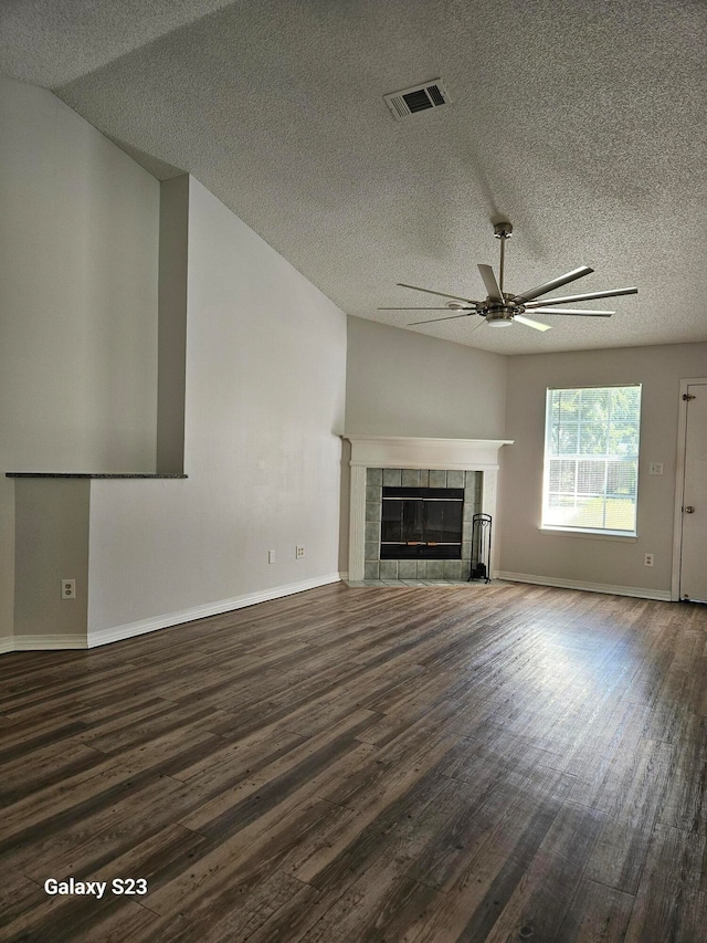 unfurnished living room featuring a tiled fireplace, ceiling fan, dark hardwood / wood-style flooring, and a textured ceiling