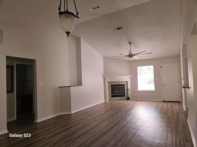 unfurnished living room featuring dark wood-type flooring, vaulted ceiling, ceiling fan, a fireplace, and a textured ceiling