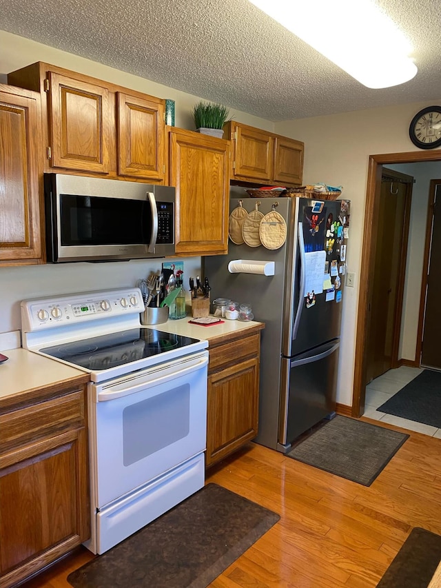 kitchen with a textured ceiling, stainless steel appliances, and light hardwood / wood-style floors