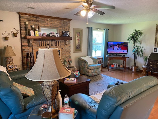 living room with ceiling fan, wood-type flooring, a textured ceiling, and a brick fireplace