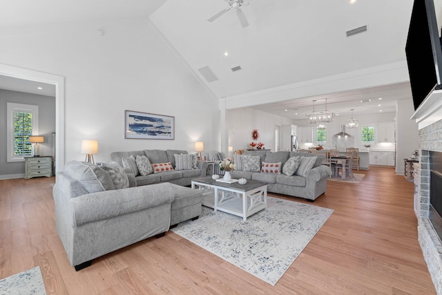 living room with plenty of natural light, a fireplace, ceiling fan with notable chandelier, and light hardwood / wood-style flooring