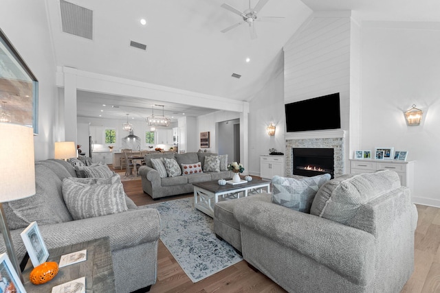 living room featuring ceiling fan, a stone fireplace, light wood-type flooring, and high vaulted ceiling