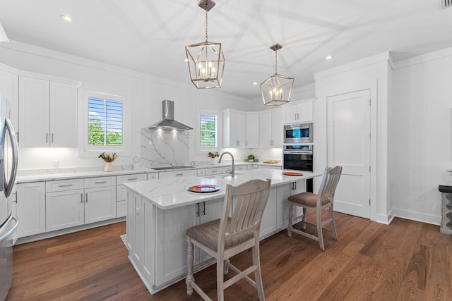 kitchen with plenty of natural light, white cabinetry, wall chimney range hood, and a kitchen island with sink