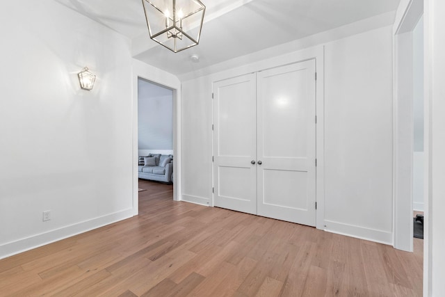 unfurnished bedroom featuring a closet, a chandelier, and light wood-type flooring