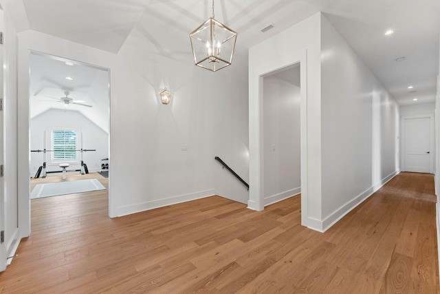 hallway with light hardwood / wood-style floors, an inviting chandelier, and lofted ceiling