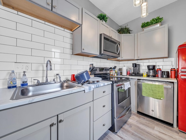 kitchen featuring gray cabinetry, sink, appliances with stainless steel finishes, tasteful backsplash, and light hardwood / wood-style floors