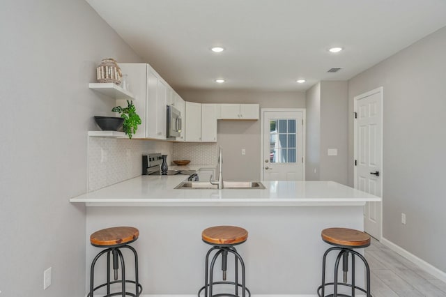 kitchen featuring kitchen peninsula, a kitchen breakfast bar, appliances with stainless steel finishes, sink, and white cabinets