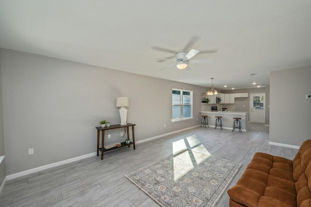 living room with ceiling fan with notable chandelier and light hardwood / wood-style floors