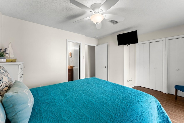 bedroom featuring hardwood / wood-style flooring, ceiling fan, a textured ceiling, and multiple closets