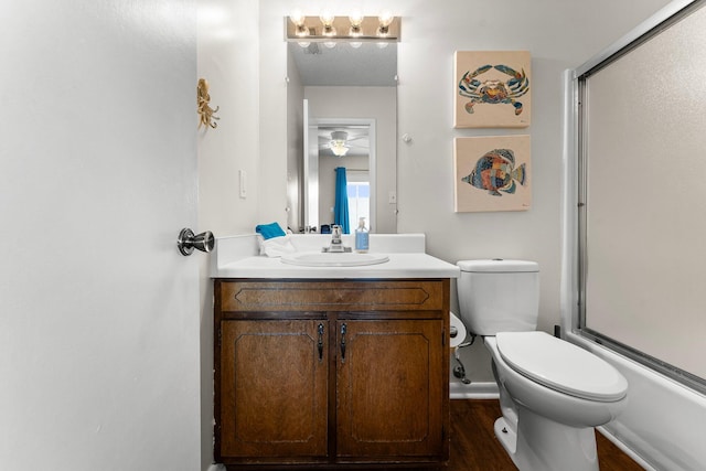 full bathroom featuring hardwood / wood-style floors, vanity, combined bath / shower with glass door, and toilet