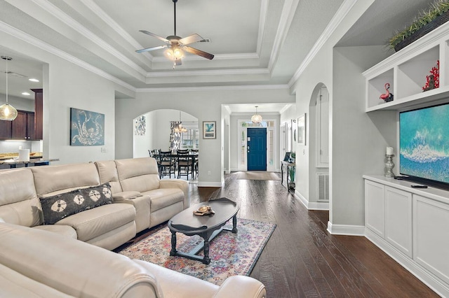 living room with ceiling fan with notable chandelier, a raised ceiling, ornamental molding, and dark wood-type flooring