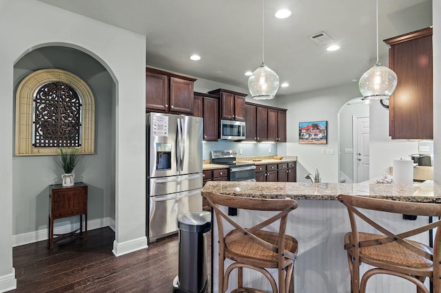 kitchen featuring dark hardwood / wood-style flooring, stainless steel appliances, light stone counters, and hanging light fixtures