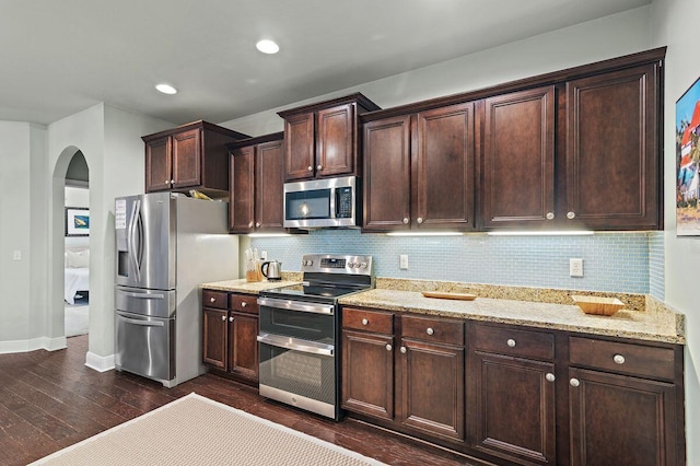 kitchen with light stone countertops, dark wood-type flooring, stainless steel appliances, decorative backsplash, and dark brown cabinets