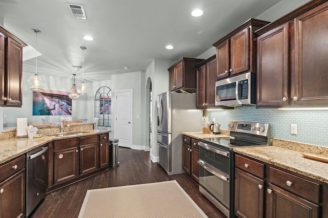 kitchen with dark brown cabinetry, appliances with stainless steel finishes, decorative light fixtures, dark hardwood / wood-style flooring, and kitchen peninsula