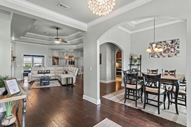 dining space with a raised ceiling, crown molding, dark wood-type flooring, and ceiling fan with notable chandelier