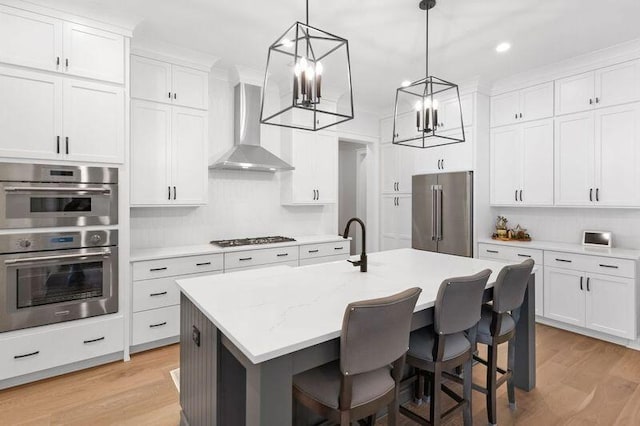 kitchen featuring white cabinets, wall chimney exhaust hood, stainless steel appliances, and a kitchen island with sink