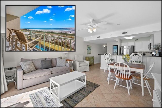 tiled living room featuring ceiling fan, a water view, and a beach view