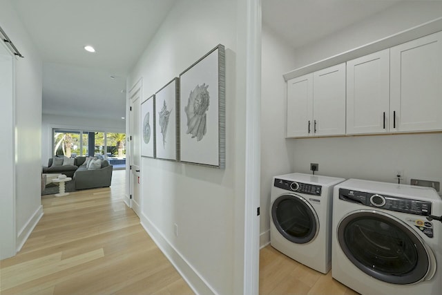 laundry area featuring a barn door, light wood-type flooring, independent washer and dryer, and cabinets