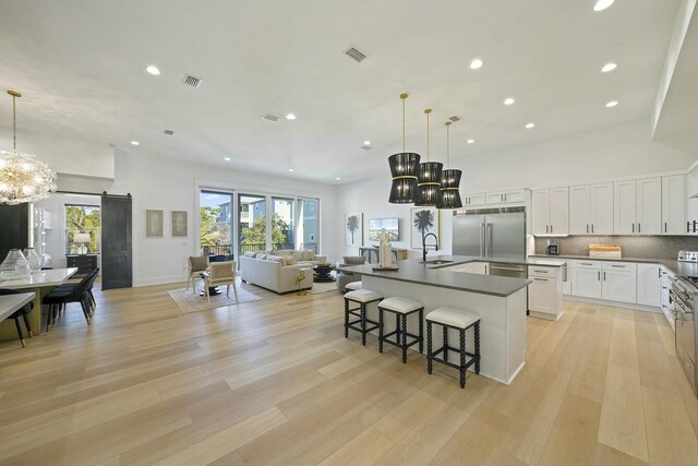 kitchen featuring white cabinets, a large island with sink, stainless steel built in fridge, and decorative light fixtures