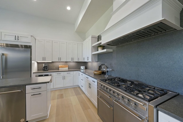 kitchen with backsplash, white cabinetry, light wood-type flooring, appliances with stainless steel finishes, and custom range hood