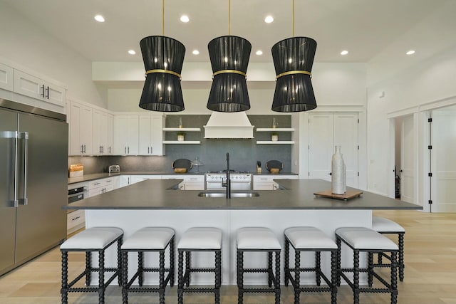 kitchen featuring white cabinetry, stainless steel built in refrigerator, sink, backsplash, and a kitchen island with sink