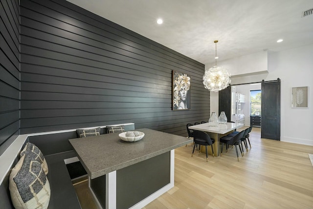 dining area with light hardwood / wood-style flooring, wood walls, a barn door, and an inviting chandelier