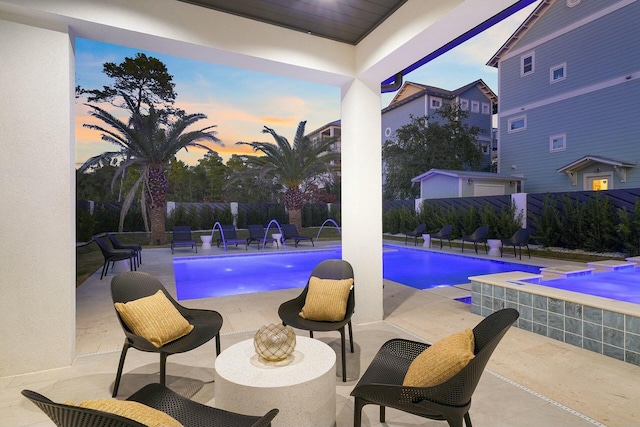 pool at dusk featuring pool water feature, an in ground hot tub, and a patio