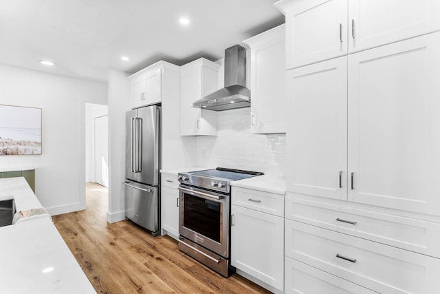 kitchen featuring white cabinetry, wall chimney exhaust hood, light hardwood / wood-style floors, and appliances with stainless steel finishes