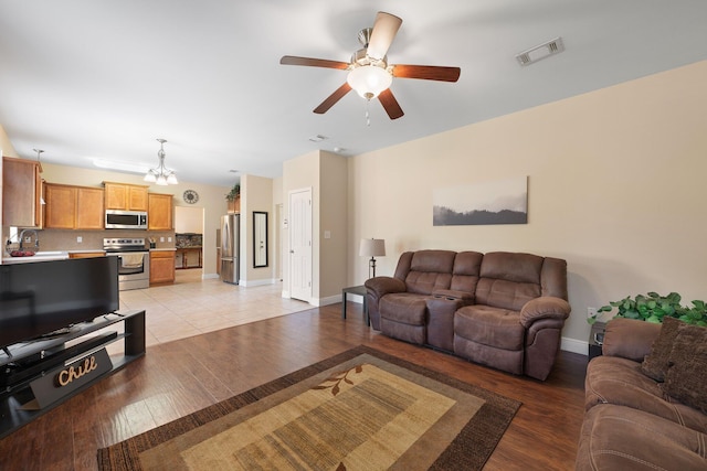 living room featuring ceiling fan with notable chandelier and light wood-type flooring