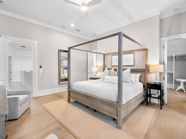 bedroom with a walk in closet, ceiling fan, crown molding, and light wood-type flooring