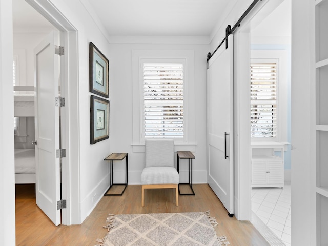 living area featuring a barn door, light hardwood / wood-style flooring, and ornamental molding