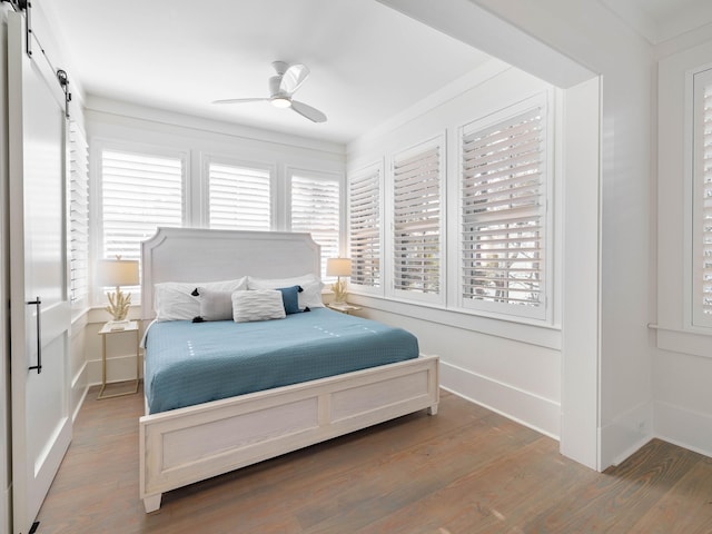 bedroom featuring wood-type flooring, a barn door, ceiling fan, and ornamental molding