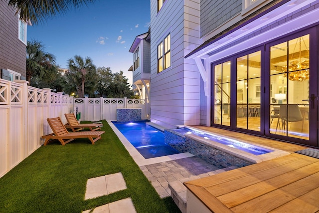 pool at dusk with pool water feature and a hot tub